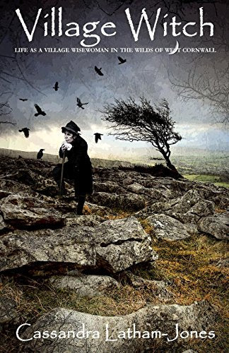 Woman in black cloak and hat standing on rocky moor with crows and tree.