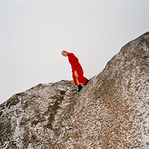Person in red dress walking up a rocky, snowy hill.