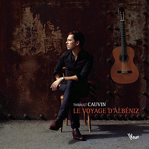 Guitarist Thibault Cauvin sits with his guitar against a textured wall.