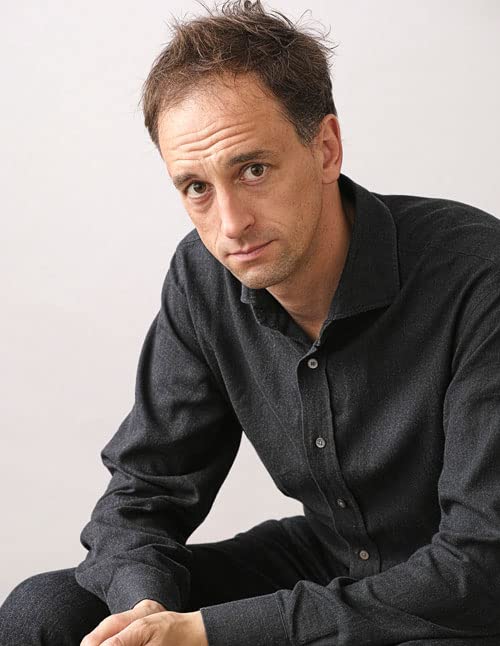 A man with short brown hair wearing a dark grey button-down shirt.