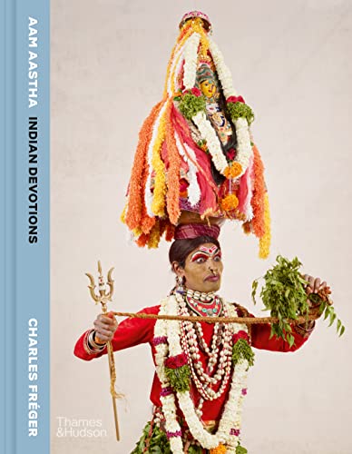 A person in traditional Indian ceremonial attire and makeup balances a large floral headpiece.