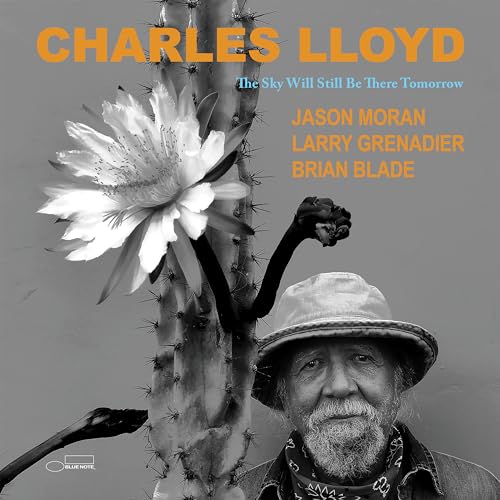 Charles Lloyd wearing a hat next to a blooming cactus on a gray background.