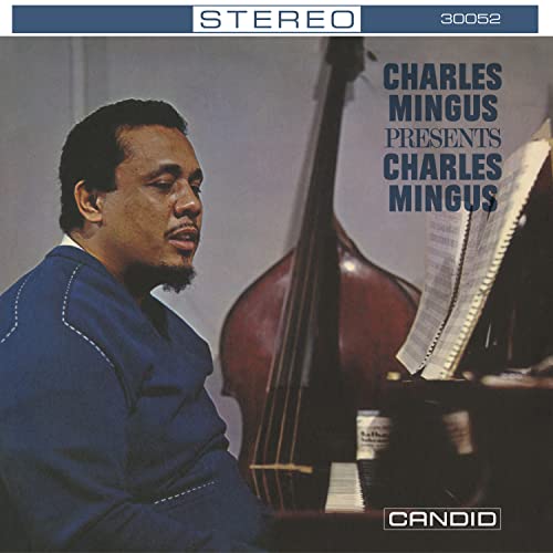 Charles Mingus sitting beside a double bass with sheet music on a stand.