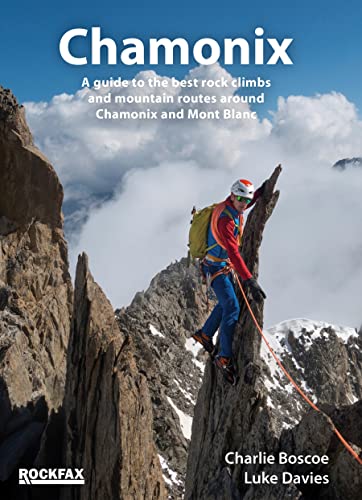 A climber on a rocky ridge with mountains and clouds in the background.