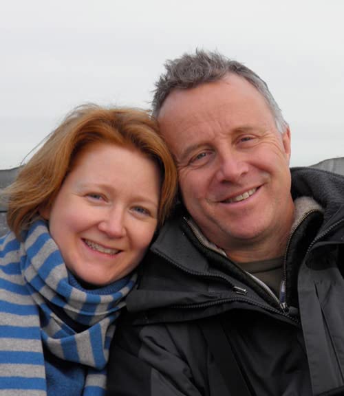 A smiling couple with heads leaning together outdoors against a pale sky.