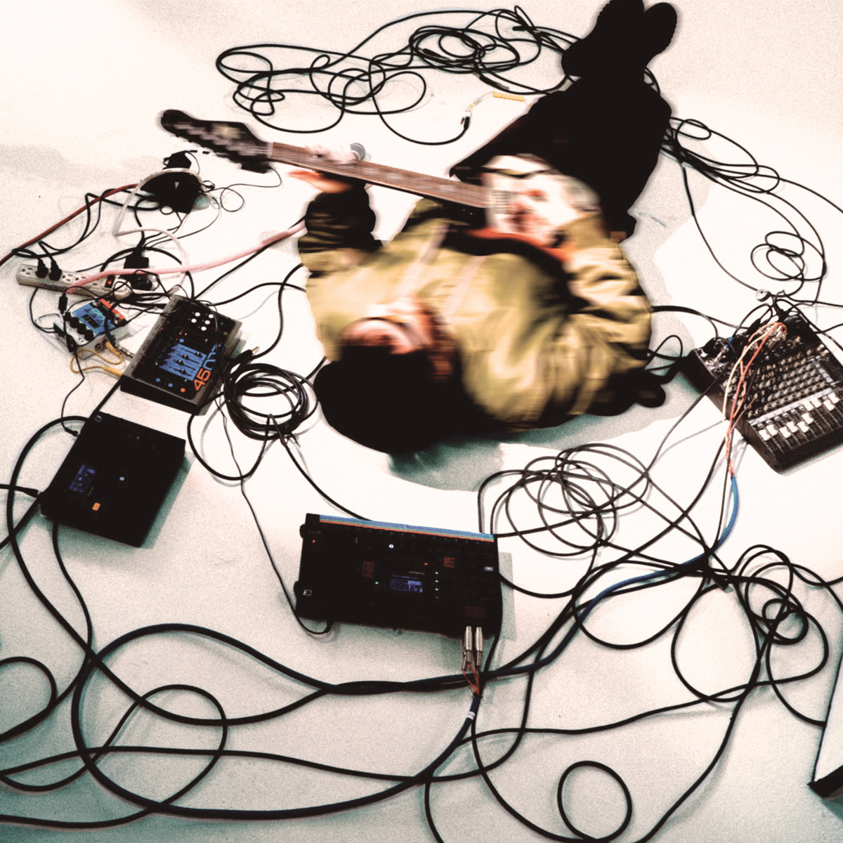 Person lying amongst guitar, effects pedals, and tangled cables.