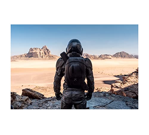 Figure in spacesuit stands on rocky desert landscape under blue sky.