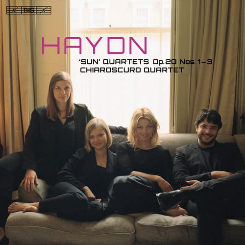 Four members of the Chiaroscuro Quartet sit on a sofa in front of a window.