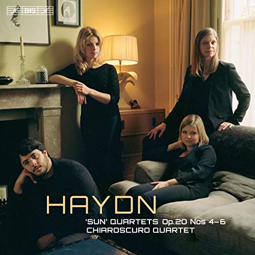Four members of the Chiaroscuro Quartet pose in a dimly lit, cozy living room.