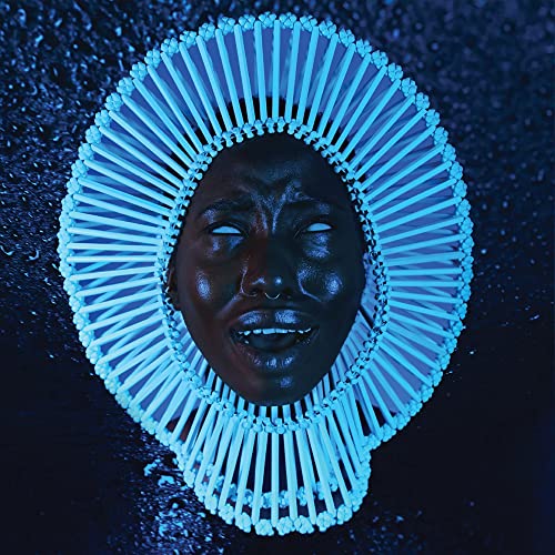 A person with white eyes wears a large, glowing blue circular headpiece against darkness.