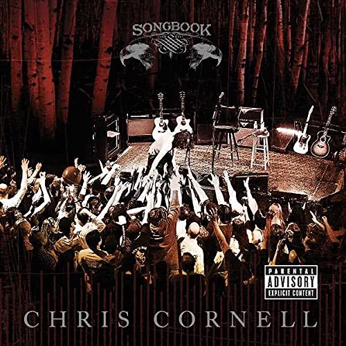 Chris Cornell performing on stage in front of a crowd with guitars and trees.