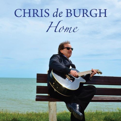 Chris de Burgh sits on a bench, playing a guitar, by the sea.