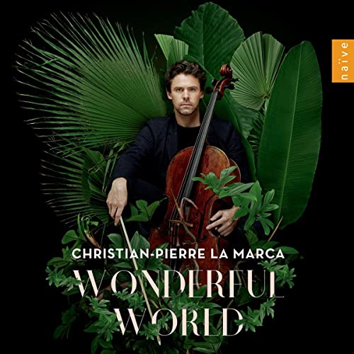 Cellist Christian-Pierre La Marca amidst lush green tropical foliage.