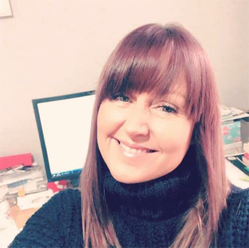 Woman with reddish-brown hair smiling at the camera, office background.