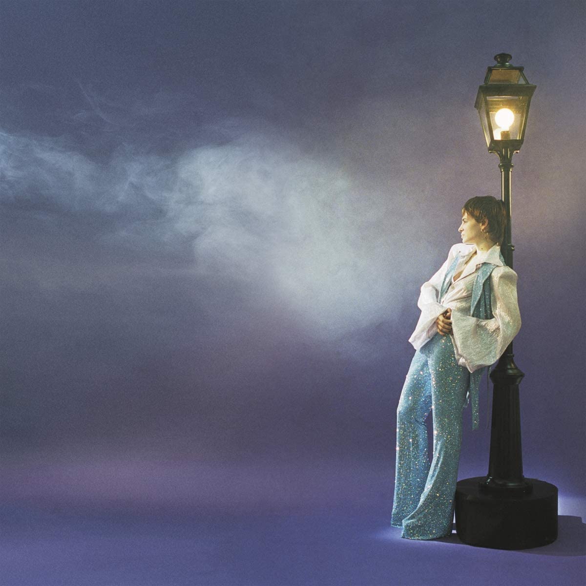 "Album cover featuring a person in a sparkly dress standing by a lit lamppost."