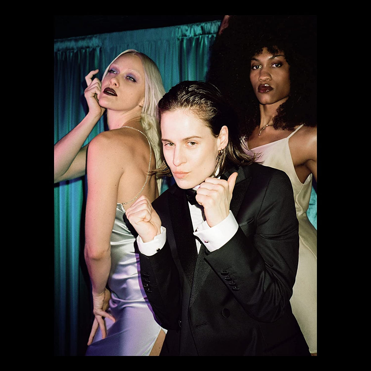 A man in a tuxedo poses with two women in evening gowns behind him.