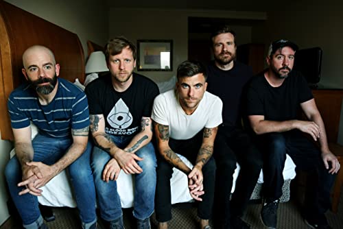 Five men, the band Circa Survive, seated on a hotel bed.