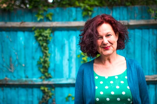 Woman with red hair smiles against a bright blue wooden fence.