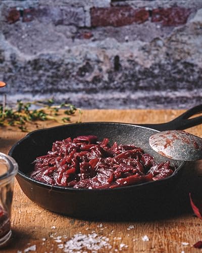 Dark red elderberry jam in a cast iron pan with herbs.