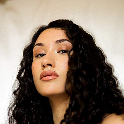 Close-up portrait of a woman with long, dark, curly hair against a white background.