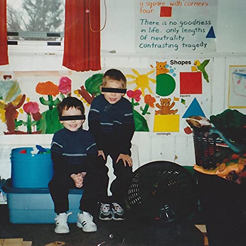 Two young children with obscured faces stand in front of colorful classroom decor.