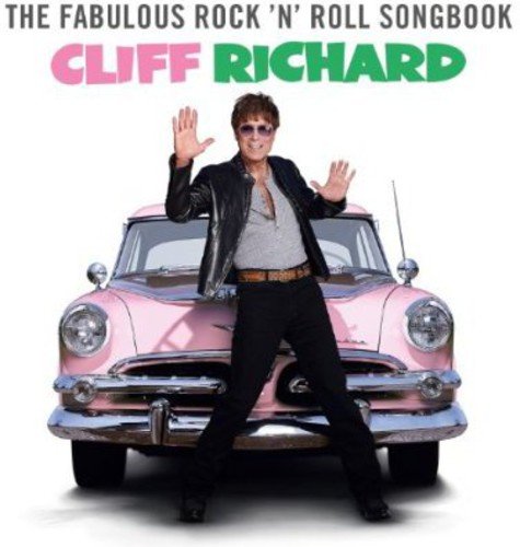 Cliff Richard standing in front of a pink vintage car, waving, on a white background.