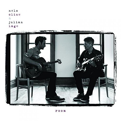 Two musicians with guitars seated facing each other by a window.
