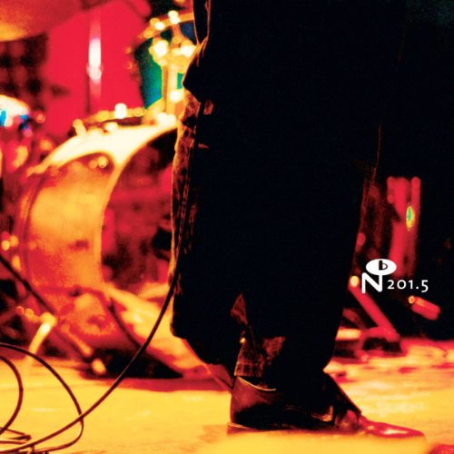 A low-angle, red-toned shot of a musician's legs and drum kit on stage.