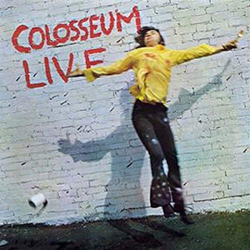 A person in a yellow shirt jumps in front of a white brick wall.