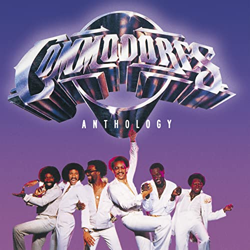 The Commodores band members in white suits pose against a purple background.