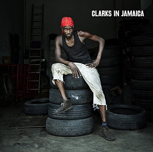 Man wearing Clarks shoes sits on tires in a garage.