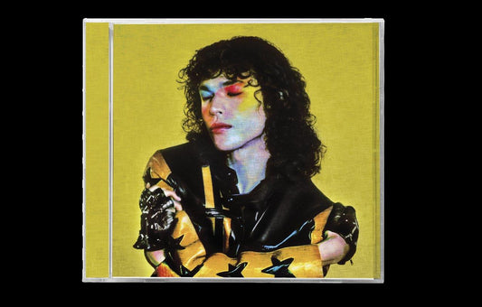 Conan Gray with curly hair and colorful makeup on a yellow background CD cover.