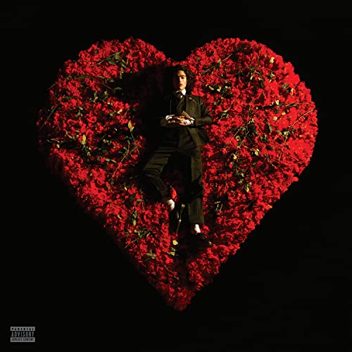 A person in a black suit lying on a large heart-shaped bed of roses.