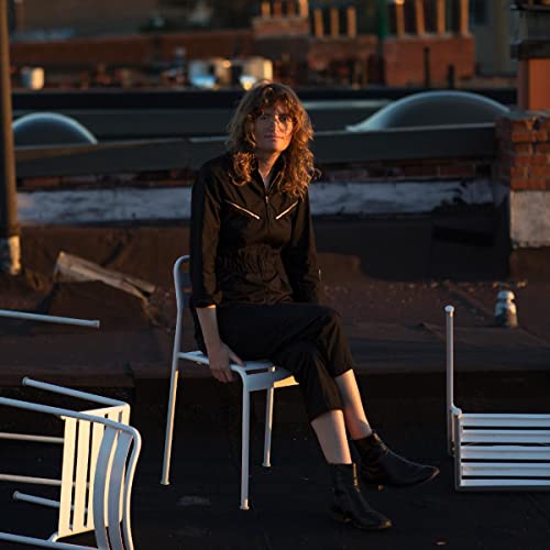 Woman with curly hair sitting on a white chair on a rooftop.