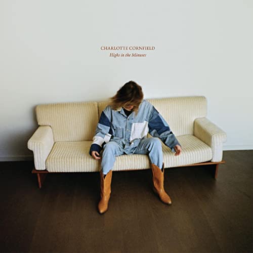 A person in denim and cowboy boots sits on a cream sofa against white walls.