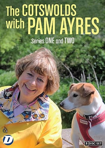 Pam Ayres smiling next to a small dog in a red harness outdoors.