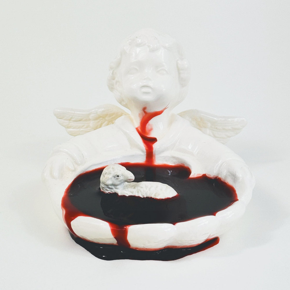 White angel statue cradling a lamb in a pool of red liquid.