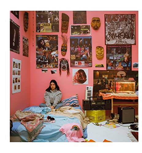 Woman sits on a bed in a room filled with posters and artifacts.
