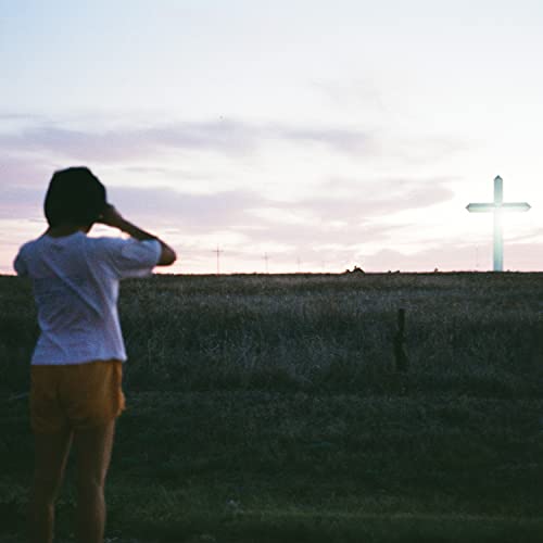 Person viewed from behind looking at a cross in a field.