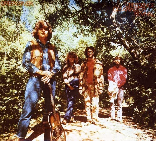 Four members of Creedence Clearwater Revival stand on a wooded path in sunlight.