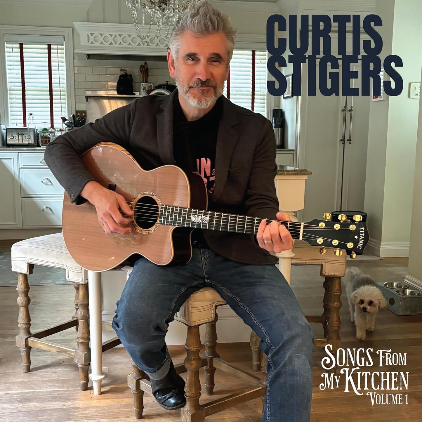 Curtis Stigers sits with an acoustic guitar in a kitchen setting.