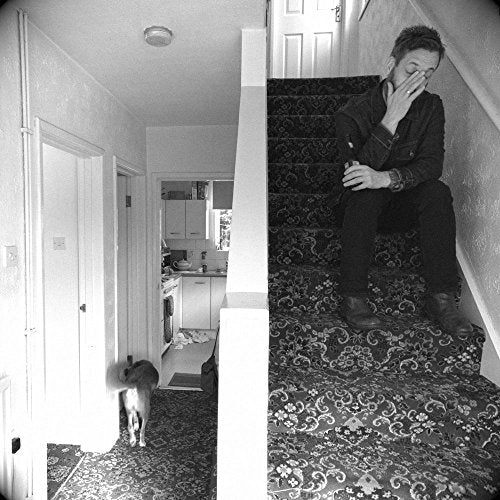 Black and white photo of a man seated on stairs, a cat below.
