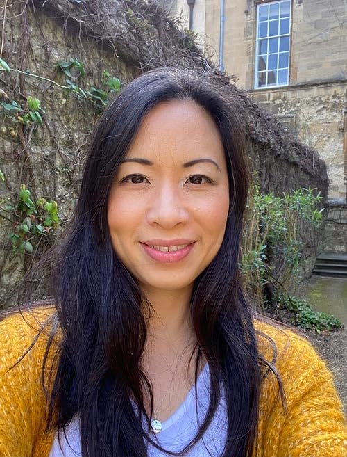Woman with long dark hair smiling, stone wall and building backdrop.