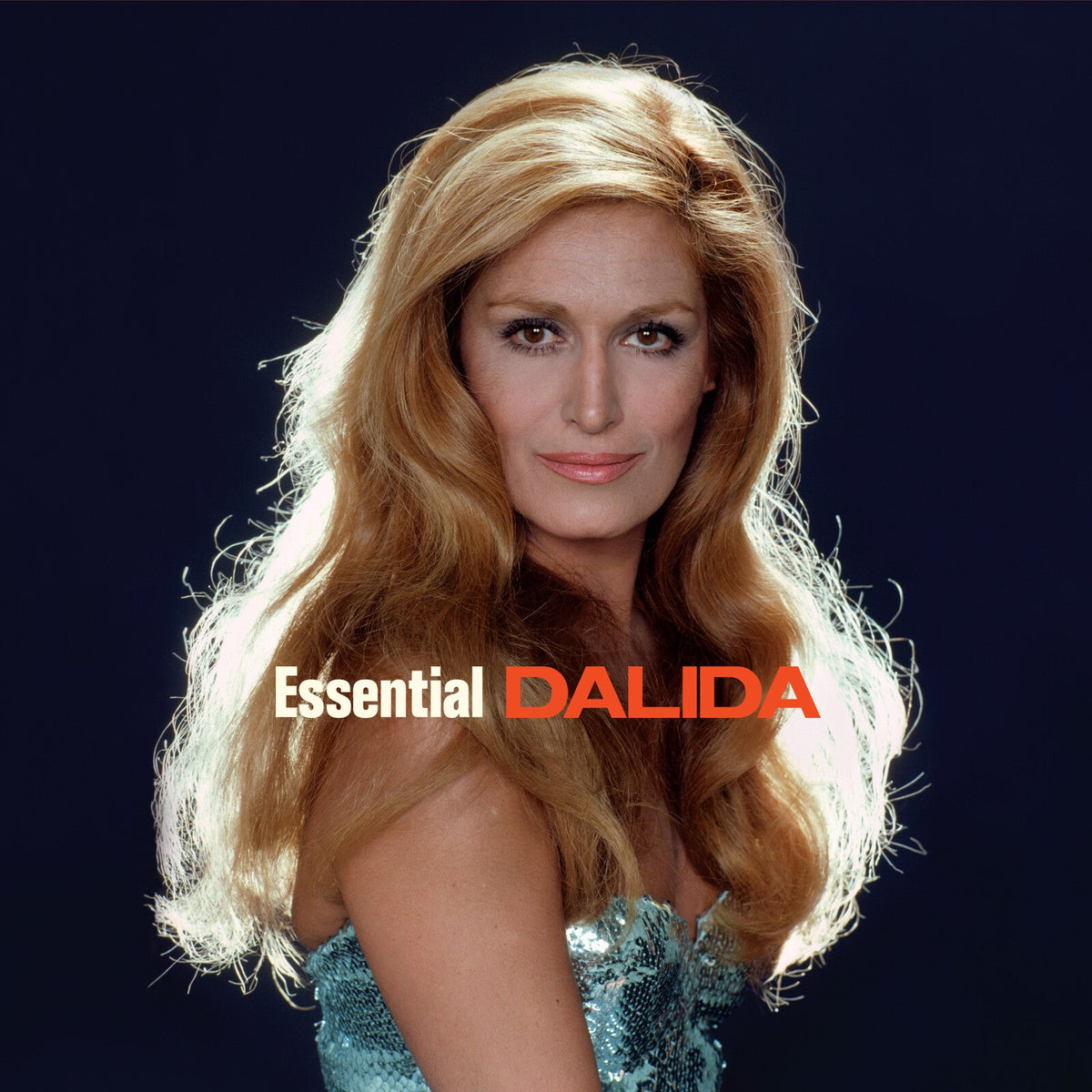 Portrait of Dalida with long blonde hair and a sequined dress on dark background.