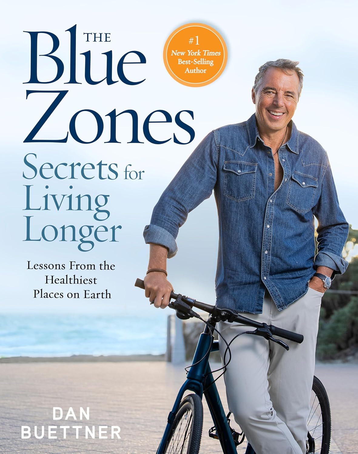 Book cover featuring Dan Buettner smiling while leaning on a bicycle by the ocean.