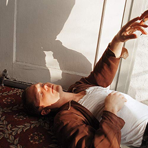 The image depicts a woman lying on a red floral-patterned rug, wearing a brown shirt and white tank top. For accessibility purposes, a suitable alt text could be: "Woman lying on a red patterned rug, wearing brown shirt."