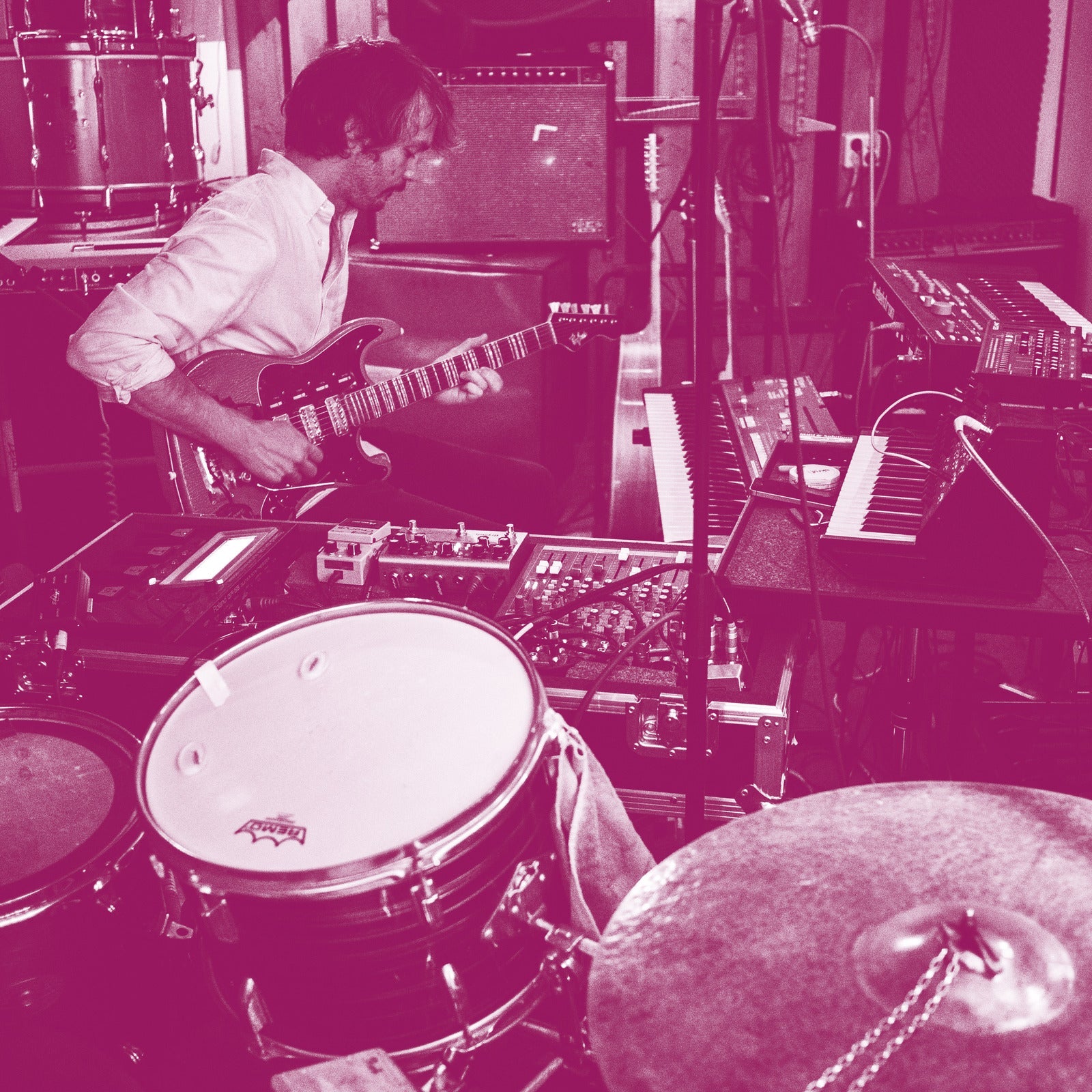 Monochrome magenta image of a man playing electric guitar in a music studio.