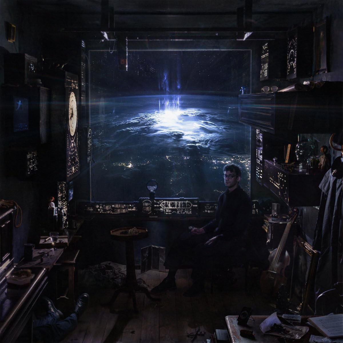 A man sits in a dark, cluttered room looking out at Earth from space.