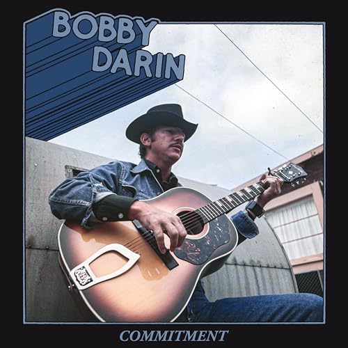 Bobby Darin in a cowboy hat playing an acoustic guitar.