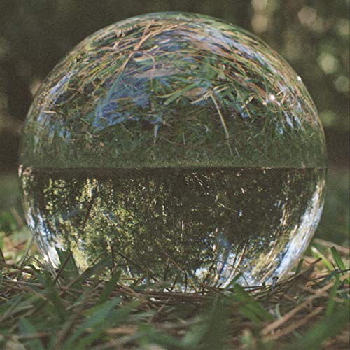 Clear glass sphere reflecting grass and trees, resting on grass.